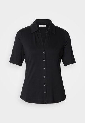 Melna īsām piedurknēm blūze, izgatavota no gludas auduma. Ievērojama ar apkakles dekoltē un pogu aizdari, kas sastāv no sešām apaļām pogām.