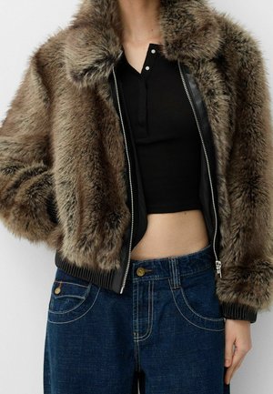Giacca bomber in pelliccia sintetica nei toni del marrone con dettagli in pelle nera, dotata di chiusura con zip e polsini a costine. Abbinata a jeans di denim blu scuro.