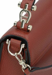 Hoek van een rode leren handtas met zilveren beslag en een opvallend sluitingsdetail. Getextureerd oppervlak met een gladde rand.