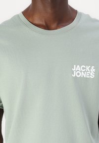 Lysegrønn bomull T-skjorte med rund hals og korte ermer. Har en hvit logo "JACK & JONES" på venstre bryst. Jevn tekstur.