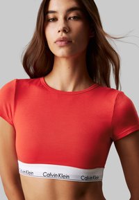 Červený bavlnený crop top s krátkymi rukávmi a bielym elastickým pásom so značkou "Calvin Klein" na leme.