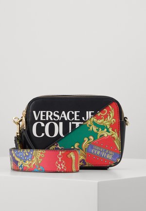 Compacte crossbodytas met zwarte achtergrond, dikke witte "Versace Jeans Couture" tekst en levendig veelkleurig barokpatroon op de riem en hoek.
