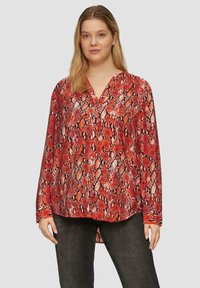 Langarmige rode blouse met een slangenprintpatroon, voorzien van een V-halslijn en een iets langere achterkant. De stof heeft een gladde textuur.