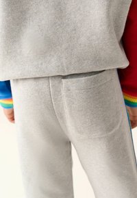 Sivé bavlnené jogger nohavice so zadnou kapsou, ktoré majú jemnú textúru a elastický pás. Pestré pruhované akcenty na rukávoch vrchu.