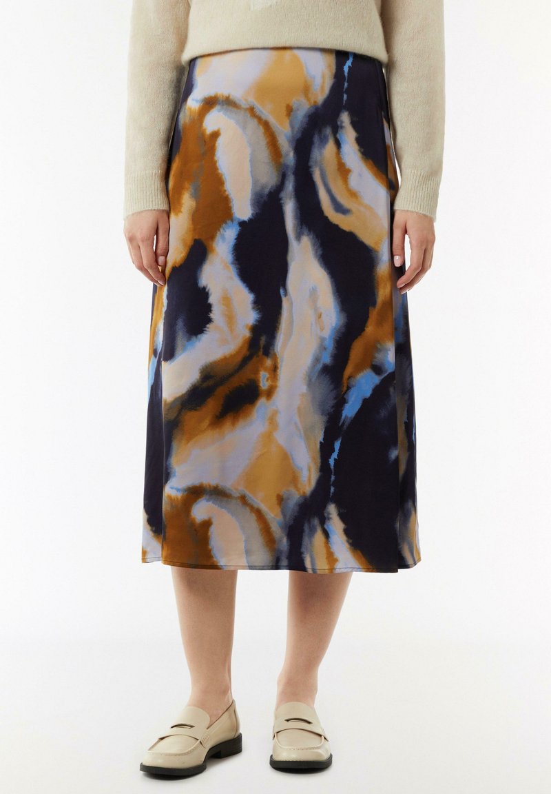 Jupe mi-longue en tissu fluide avec un motif abstrait bleu, orange et noir. Forme évasée, texture lisse, portée avec des mocassins.