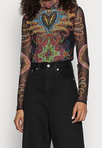 Sheer black long-sleeve top with colorful intricate patterns, featuring a high neck and fitted silhouette, paired with high-waisted black jeans.