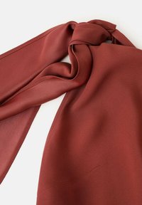 Jedwabny szalik w głębokim rdzawym kolorze, o gładkiej fakturze i widocznych przeszyciach wzdłuż krawędzi, elegancko ułożony.