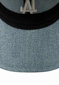Gorra de béisbol de mezclilla con visera negra, que presenta un patrón de mezclilla azul claro y un logo bordado gris en la parte frontal.