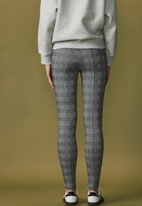 Tæt siddende gråternede leggings med et strømlinet design og strækbart stof, parret med sorte og hvide træningssko, set bagfra.