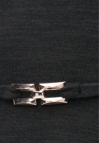 Detailní záběr na lesklou obdélníkovou kovovou sponu, která zapíná černý pletený pásek.