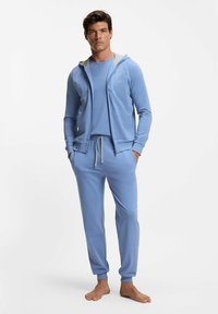 Ensemble de sport bleu en tissu doux. Comprend un sweat à capuche zippé avec des accents gris et un pantalon assorti avec une taille à cordon.