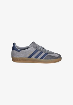 Sneaker Adidas Gazelle grigia con strisce blu navy, suola in gomma, texture in camoscio e scritta dorata "GAZELLE" sul lato.
