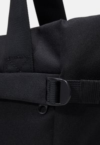 Primo piano di una tracolla di stoffa nera con una fibbia in plastica e dettagli della maniglia cucita.