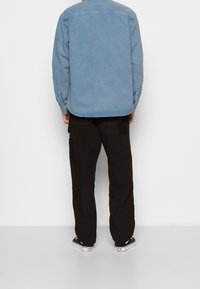 Camicia in denim azzurro chiaro con dettagli bottonati, abbinata a pantaloni cargo neri con tasche laterali. Indossata con scarpe bianche e nere.