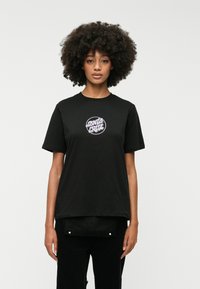 Μαύρο βαμβακερό μπλουζάκι με κοντά μανίκια, διακοσμημένο με ένα κυκλικό ροζ και λευκό γραφικό λογότυπο στο στήθος. Απλός, χαλαρός σχεδιασμός.