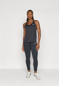 Ensemble de sport composé d'un débardeur gris foncé et de leggings noirs, tous deux en tissu lisse ; accompagné de baskets grises et blanches.