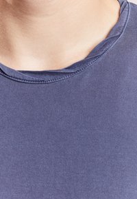 Námořnická modrá tričko s kulatým výstřihem vyrobené z hladké bavlněné tkaniny. Má jednoduchý design s volným střihem a jemnými detaily šití.