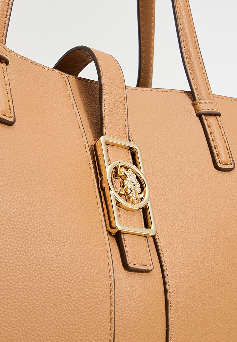 Borsa a mano in pelle marrone chiaro con una superficie liscia, doppi manici e un accento in metallo dorato con dettaglio del logo circolare.