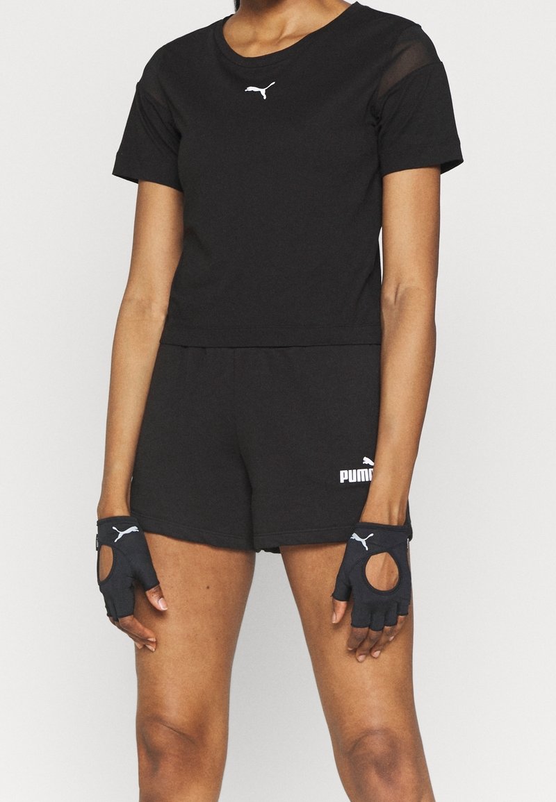 Černý sportovní outfit skládající se z trička s krátkým rukávem, šortek a rukavic bez prstů s síťovinovými detaily a bílým logem.