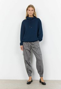 Sudadera con capucha de color azul marino con cordones, combinada con pantalones cargo grises con puños elásticos y bolsillos laterales. Zapatos planos negros completan el conjunto.