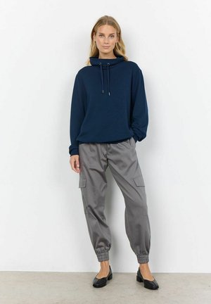 Merevaigusega kapuutsiga sweatshirthallid kapsas püksid, millel on elastsed varrukad ja küljetaskud. Mustad lamedad jalatsid lõpetavad selle väljanägemise.