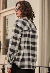 Černobílá kostkovaná flanelová košile s dlouhými rukávy, manžetami na knoflíky a špičatým límcem, s volnějším střihem a strukturovanou tkaninou.