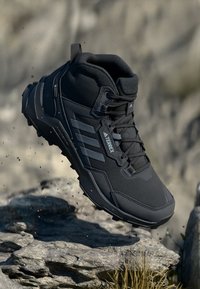 Czarne buty trekkingowe z teksturowaną cholewką, wyściełanym kołnierzem i gumową podeszwą. Posiadają logo w postaci trzech pasków oraz wzmocniony nos dla trwałości.