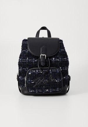 Mochila pequeña texturizada en negro y azul marino con bolsillo frontal, cierre de solapa, detalle de hebilla y asa superior sobre fondo blanco.