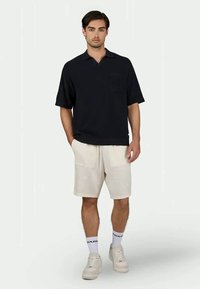 Polo shirt a manica corta di colore blu navy con taschino, abbinato a pantaloni corto crema e sneakers leggere, caratterizzato da un tessuto testurizzato e una vestibilità rilassata.