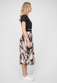 Haut noir à manches courtes associé à une jupe longueur genoux affichant un motif abstrait en beige, noir et blanc, complétée par des baskets blanches.