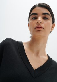 Black V-neck sweater with a soft texture and ribbed collar, showcasing a fitted design. The background is plain and neutral.