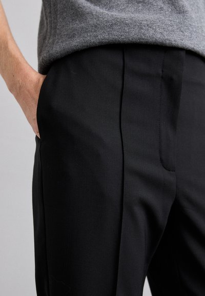 Black tailored trousers with a smooth texture, featuring front pleats and side pockets, paired with a gray knit sweater at the waist.