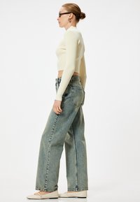 Maglia a manica lunga a costine gialla chiara abbinata a jeans larghi in denim blu a vita alta e ballerine chiare. Tessuti testurizzati.