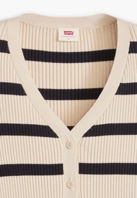 Beżowy prążkowany kardigan z granatowymi poziomymi paskami. Posiada dekolt w serek, trzy guziki oraz metkę z napisem „Levi’s”. Rozmiar S.