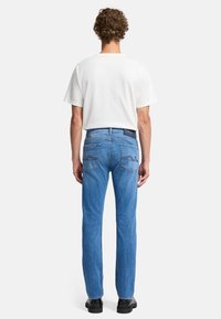 Niebieskie dżinsy z prostą nogawką, pięcioma kieszeniami i widocznymi tylnymi kieszeniami z zakrzywionymi detalami przeszyć. W połączeniu z białą koszulą.