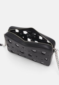 Borsa a mano in pelle nera con design geometrico ritagliato, chiusura con zip argentata, tracolla a catena e dettagli interni lucidi. Superficie texturizzata.