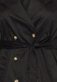 Manteau noir croisé à double boutonnage avec ceinture en tissu, doté de boutons dorés, d'une texture lisse et d'un col structuré.