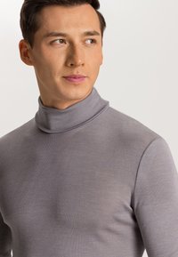 Grå polotröja i ribbat material, med en åtsittande design och hög krage. Tyget verkar mjukt och lätt.