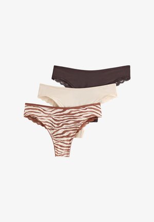 Femme debout pieds nus contre un mur blanc, portant un soutien-gorge marron foncé bordé de dentelle et une culotte taille haute assortie.