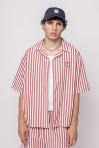 Rødt og hvitt stripete kortermet skjorte med knappelukking, brukt over en hvit tank top. Kombinert med en marineblå caps og sølvkjede.