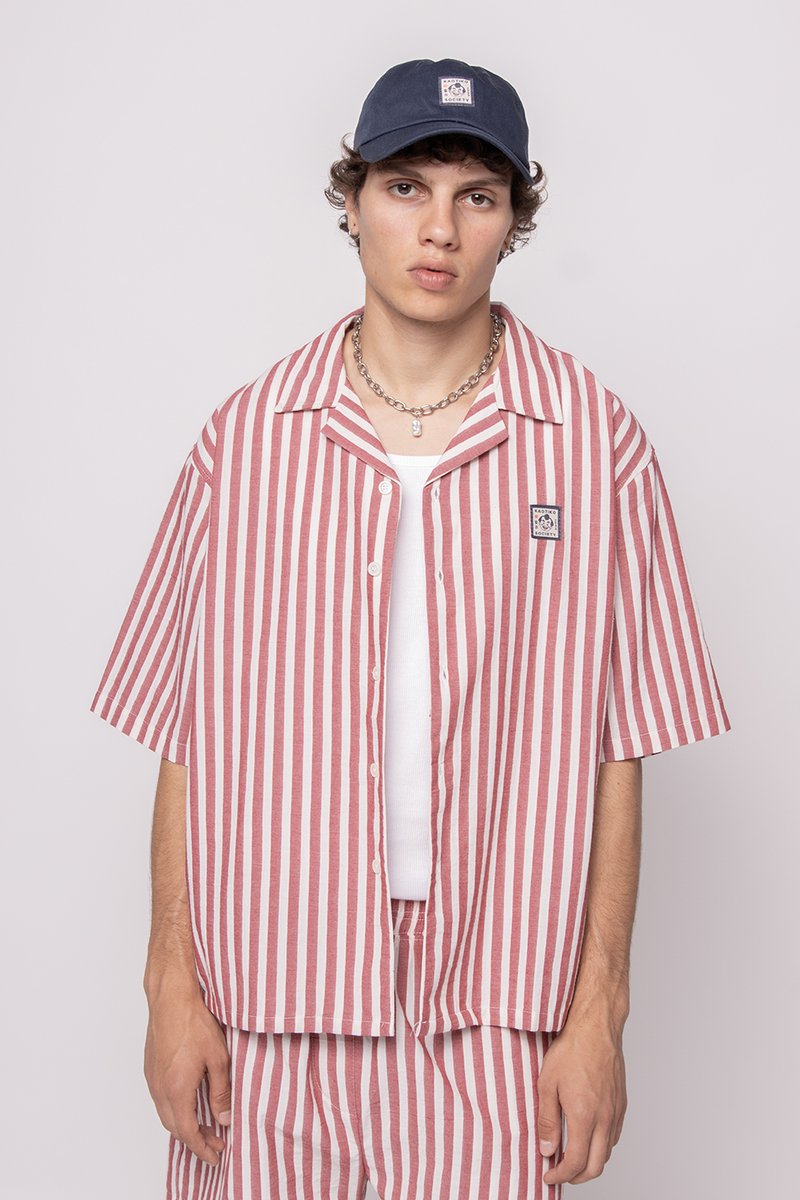 Rødt og hvitt stripete kortermet skjorte med knappelukking, brukt over en hvit tank top. Kombinert med en marineblå caps og sølvkjede.