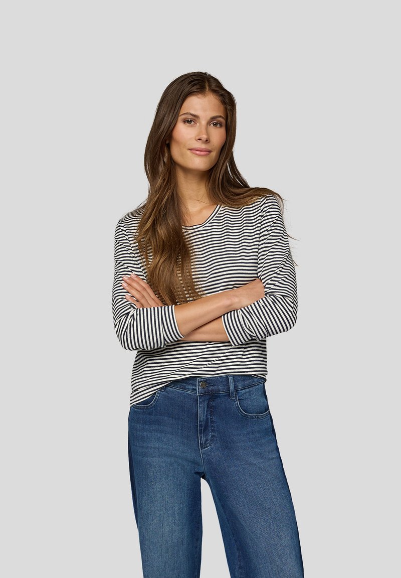 Gestreiftes Langarmshirt in Schwarz und Weiß, kombiniert mit blauen Jeans. Das Shirt hat einen runden Ausschnitt und enganliegende Ärmel.