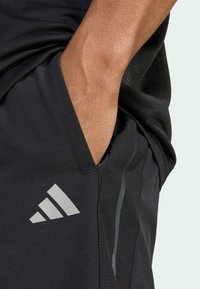Sorte fitnessshorts med en glat tekstur, prydet med et sølvfarvet adidas-logo og sidelomme. Designet inkluderer kontraststing og mesh-detaljer.