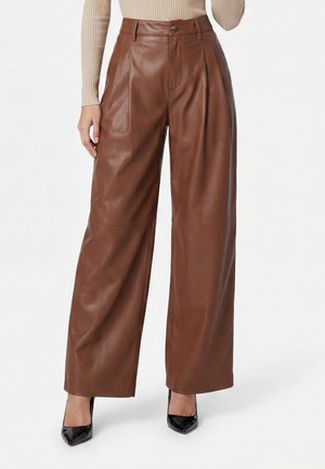 High-waist wide-leg brown leather pants worn with black pointed-toe heels and a beige ribbed top.