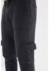 Cargo kalhoty vyrobené z černého denim materiálu, s bočními kapsami na knoflíkové zapínání, hladkým povrchem a rovnými nohavicemi.