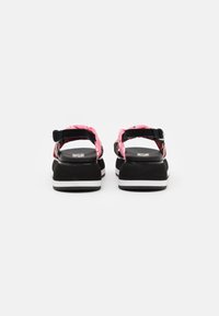 Black platform sandals with pink patterned straps and adjustable buckle. Features a white and black sole, designed for comfort and support.