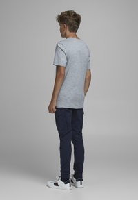 Grå bomullst-shirt med korta ärmar, tillsammans med marinblå cargobyxor. Sneakers är vita med marinblå och röda detaljer. Bakgrunden är neutral.