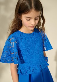 Blauw kanten top met bloempatronen en korte mouwen, voorzien van ingewikkelde borduursels, gecombineerd met een gladde blauwe rok.