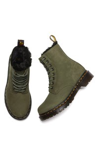 Olijfgroene veterschoenen met zwarte bontvoering, gele stiksels op dikke zwarte zolen en gelabelde hiellussen, getoond vanuit boven- en zijkant.