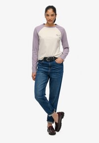 Camisa de manga larga con cuerpo crema y mangas raglán lavanda, combinada con jeans azul medio y zapatos oscuros de tipo slip-on.
